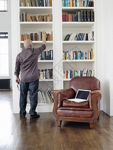 成年男子从书架上取书的全长后方视图架子地面笔记本男性退休男人人员房间扶手椅闲暇图片