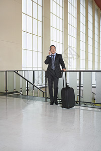 一名在机场使用移动电话的商务人士长整个身 满身都是生意人旅游婴儿中年旅行工人手提箱套装人士男人大堂图片