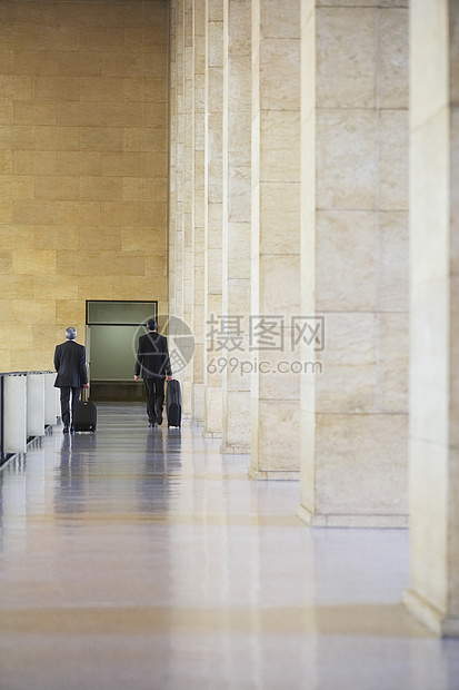 两名商务人士在机场前厅拖车行李的完整后方全景图片