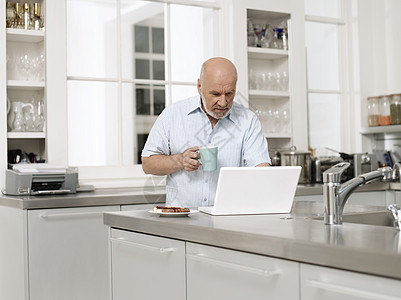 在厨房用手拿着咖啡杯的笔记本电脑图片