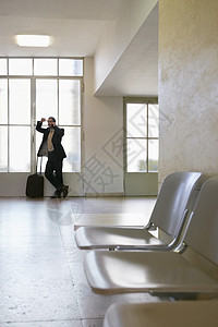 一名在机场使用移动电话的商务人士长整个身 满身都是生意人椅子男性电话行李工人飞机场倾斜手提箱手机商业图片