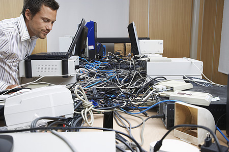 一名男性办公室工人的侧面观 他看着连接办公室电脑和打印机的电线混乱图片