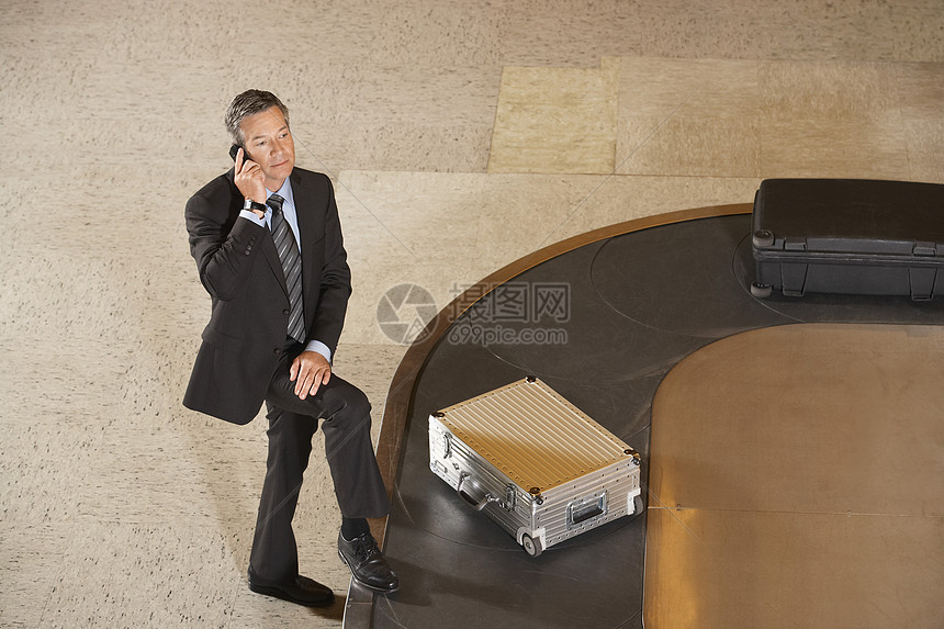 商务人士在机场的旋转木轮上使用随行李携带移动电话人士沟通商务地面木马沉思水平长椅旅行中年图片