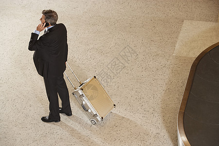 机场用行李木轮手提电话对一个拥有手提箱的商务人士全长视线高处图片