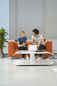 办公室接待室用笔记本电脑在橙色沙发上使用多族裔夫妇的全长种族商业装饰橙子风格金发女郎互联网成人房间会议图片
