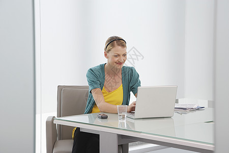 办公室办公桌上使用笔记本电脑微笑的年轻妇女图片