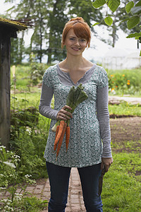 一位微笑的年轻女子在花园里拿着胡萝卜的肖像图片