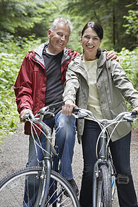 在森林里骑自行车的幸福成熟男子和中年女子的肖像图片
