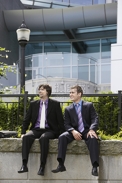 坐在办公室外墙上的两名青年商务人士全身在办公室外图片