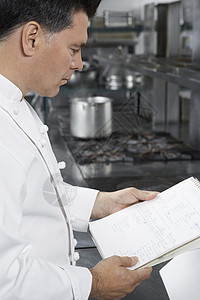 中年男厨师在厨房阅读食谱的侧面视图工作用具男性训练商业工作服职员餐厅职业男士图片
