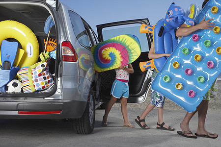 父亲和两个孩子从汽车上卸下海滩配件图片