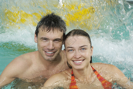 游泳池中一对微笑的年轻夫妇的近相肖像图片