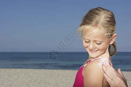 在海滩上给笑着女儿擦防晒霜的手贴紧图片