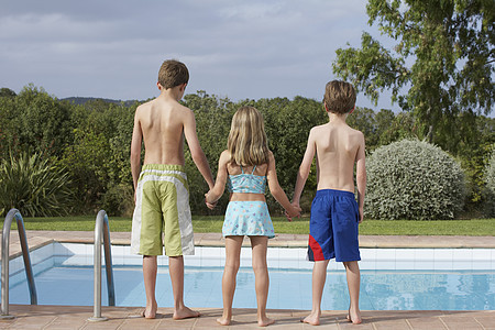两个兄弟和一个姐妹在游泳池边缘的全长后方视线图片