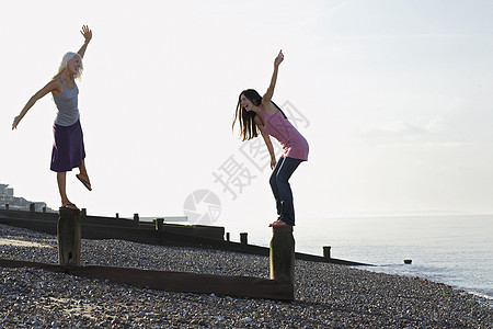 两名年轻妇女在沙滩上平衡木制断浪器图片