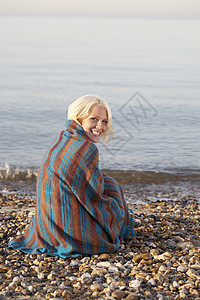 美丽的年轻女人的肖像 被裹在毯子里坐在沙滩上图片
