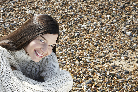 坐在沙滩上穿着毛衣的快乐年轻女子的肖像图片