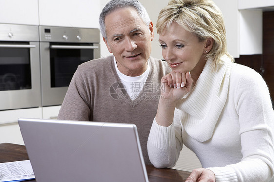 在厨房桌上使用笔记本电脑的快乐中年夫妇图片