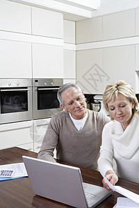 快乐的中年夫妇在厨房桌上用笔记本电脑计算家庭财务女性桌子文档讨论文书工作技术沟通女士团结图片