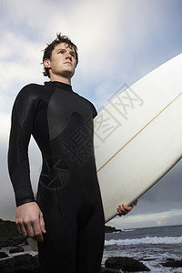 男子在海滩低角度视图上持冲浪板图片