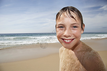 穿着沙沙在海滩上笑脸的无衬衣男孩近身肖像图片