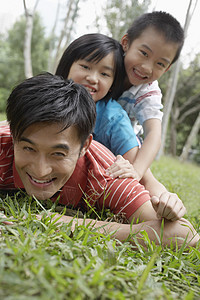 父亲和孩子躺在公园草地上的孩子玩耍的父亲的肖像图片