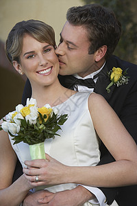 格隆亲吻新娘 从后面 当她拿着花束图片