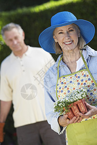 一位快乐的年长女子拿着花盆与背景中的男子相提并论的肖像图片