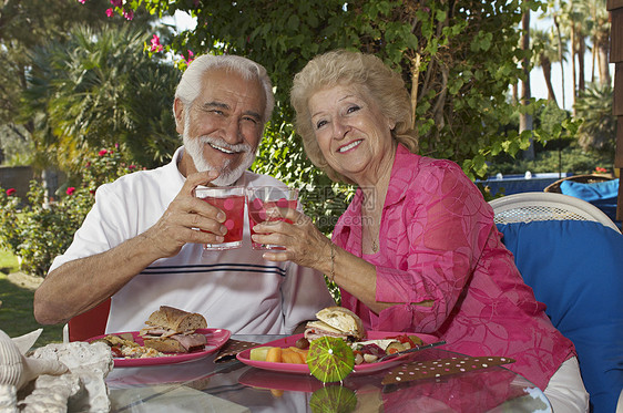 一对快乐的老年情侣在户外桌边吃饭时 喝着饮料杯敬酒的肖像图片