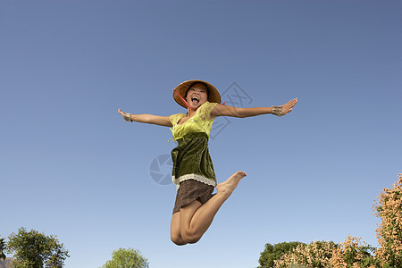 充满欢乐的亚洲女人 用双臂向蓝天伸展跳跃图片