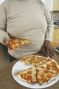 在厨房柜台拿着一块披萨的肥胖男子的中产体图片