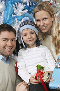 一对快乐的年轻夫妇的肖像 带着儿子在圣诞树前拿着礼物图片