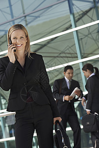 与背景同事使用手机的漂亮商业女商务人士AC 1衣冠商务电话一个人细胞中年人女士微笑办公楼男子图片