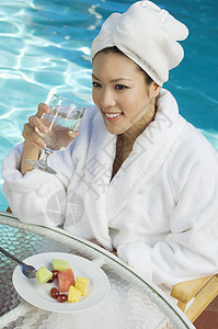 一位美丽的亚洲女性在泳池旁 握着一杯水的高角度视角图片