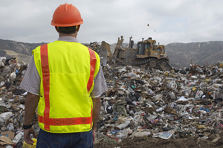 在垃圾填埋场看挖掘作业废物的工人中年人工作制服卡车头盔运输男子背心安全挖掘机图片