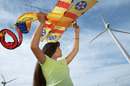 在风力农场玩飞机风筝的年轻女孩图片