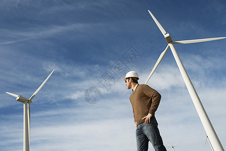 一名男性工程师在风力农场与涡轮机对面站立的低角度视角图片