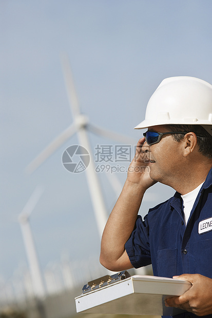 在风力农场使用移动电话剪贴板的男工程师太阳镜安全帽活力手机涡轮机肩膀男人细胞电话中年图片