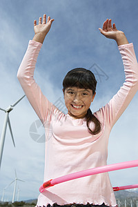 一个快乐的年轻女孩在风力农场玩呼啦圈的低角度景象肖像图片