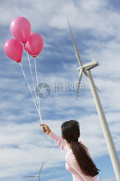 一个年轻女孩在风力农场玩粉色气球的近视图片