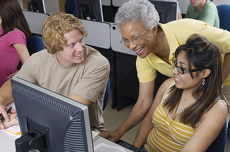 帮助工作在计算机教室的两名学生的老师微笑女性智力中年大学生服装学费设备年轻人瞳孔图片