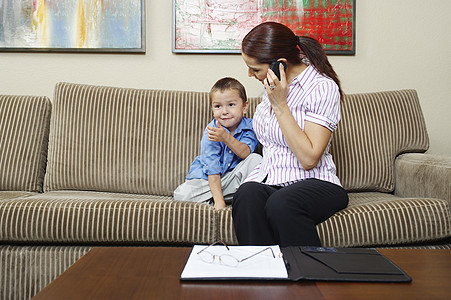 商业妇女在家里用手机通信时看着儿子 看儿子;女商务人士图片