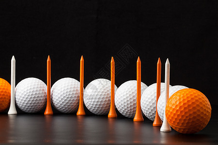 黑色背景的高尔夫球球座材料白色圆圈橙子运动木头桌子图片