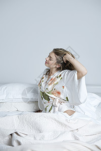 穿着睡衣在床上伸展的年轻女青年长发微笑丝绸浴衣卧室女士图案女子头发羽绒被图片