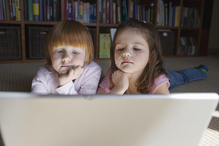 女孩(5-6)躺在地板上 用笔记本电脑在下巴上用手思考图片