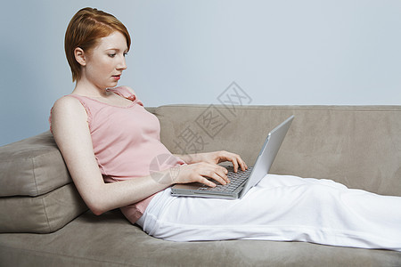 在沙发上使用笔记本电脑的妇女影棚黄色背心成人一人工作室头发双肩女士女子图片
