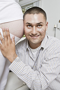 男人对怀孕妇女的腹部带着头的微笑图片