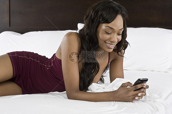 睡在床上的中年成年妇女微笑女性黑发沟通内衣使用酒红色短信卧室手肘图片