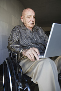 使用膝上型电脑坐轮椅的老年男子图片