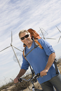 在风力农场附近骑自行车的老年男子闲暇微笑退休自然资源倾斜自由毛衣能源生态旅游休闲图片